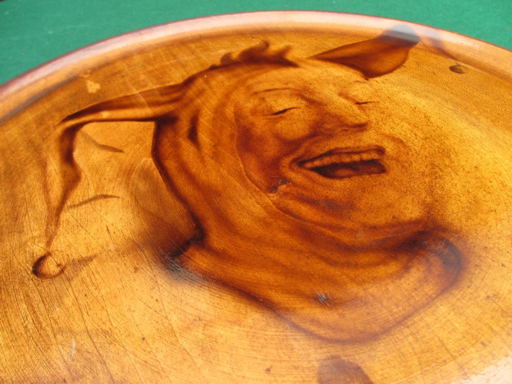 A circular turned mahogany wooden tray featuring a central branded portrait of a laughing jester wearing a cap with bells. View IV