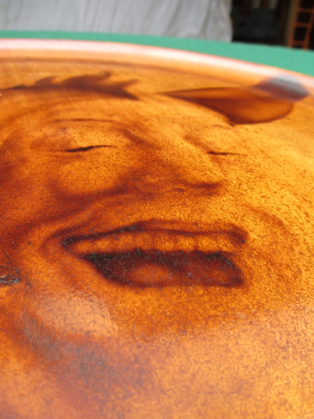 A circular turned mahogany wooden tray featuring a central branded portrait of a laughing jester wearing a cap with bells. View VIII
