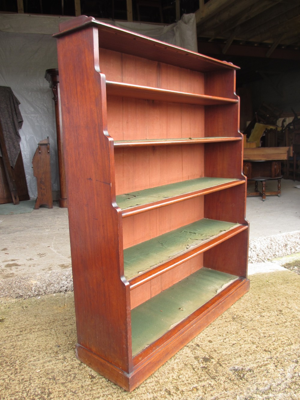 A tall 19th-century mahogany waterfall bookcase featuring six graduating open shelves with green fabric lining and a shaped gallery top.