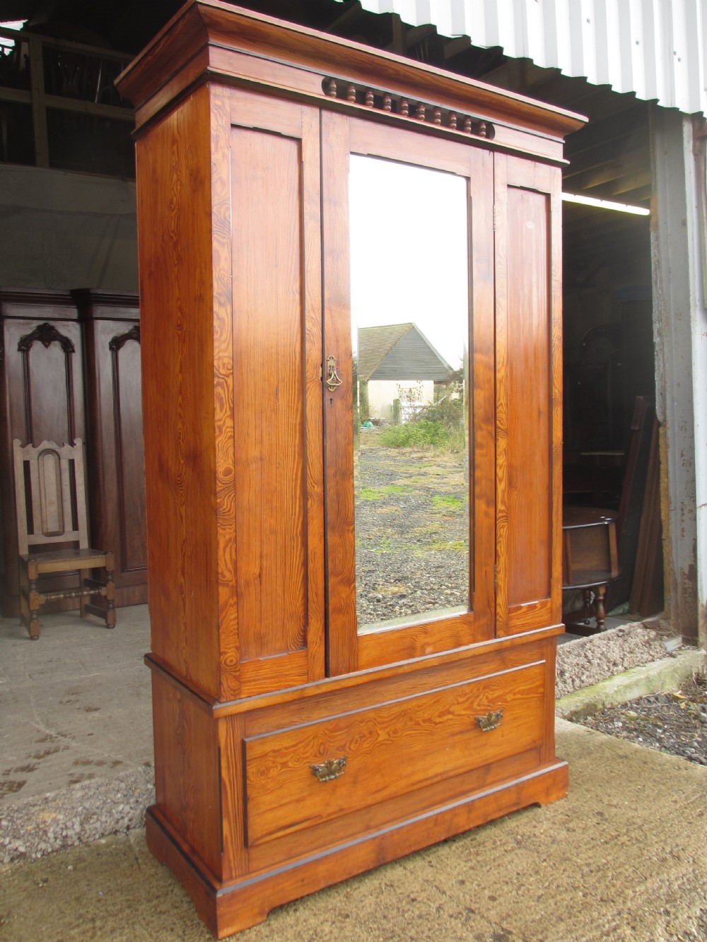 A Victorian pitch pine freestanding wardrobe featuring a central bevelled mirror door, upper spindle gallery, panelled sides, and a single lower drawer. View III