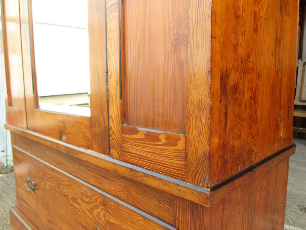 A Victorian pitch pine freestanding wardrobe featuring a central bevelled mirror door, upper spindle gallery, panelled sides, and a single lower drawer. View VI
