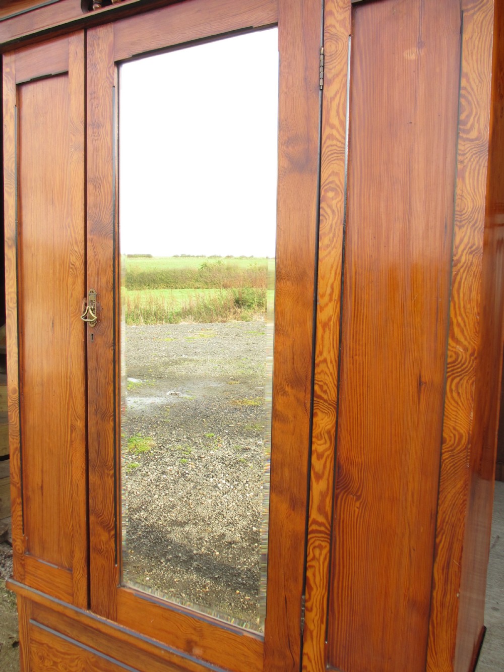 A Victorian pitch pine freestanding wardrobe featuring a central bevelled mirror door, upper spindle gallery, panelled sides, and a single lower drawer. View VIII