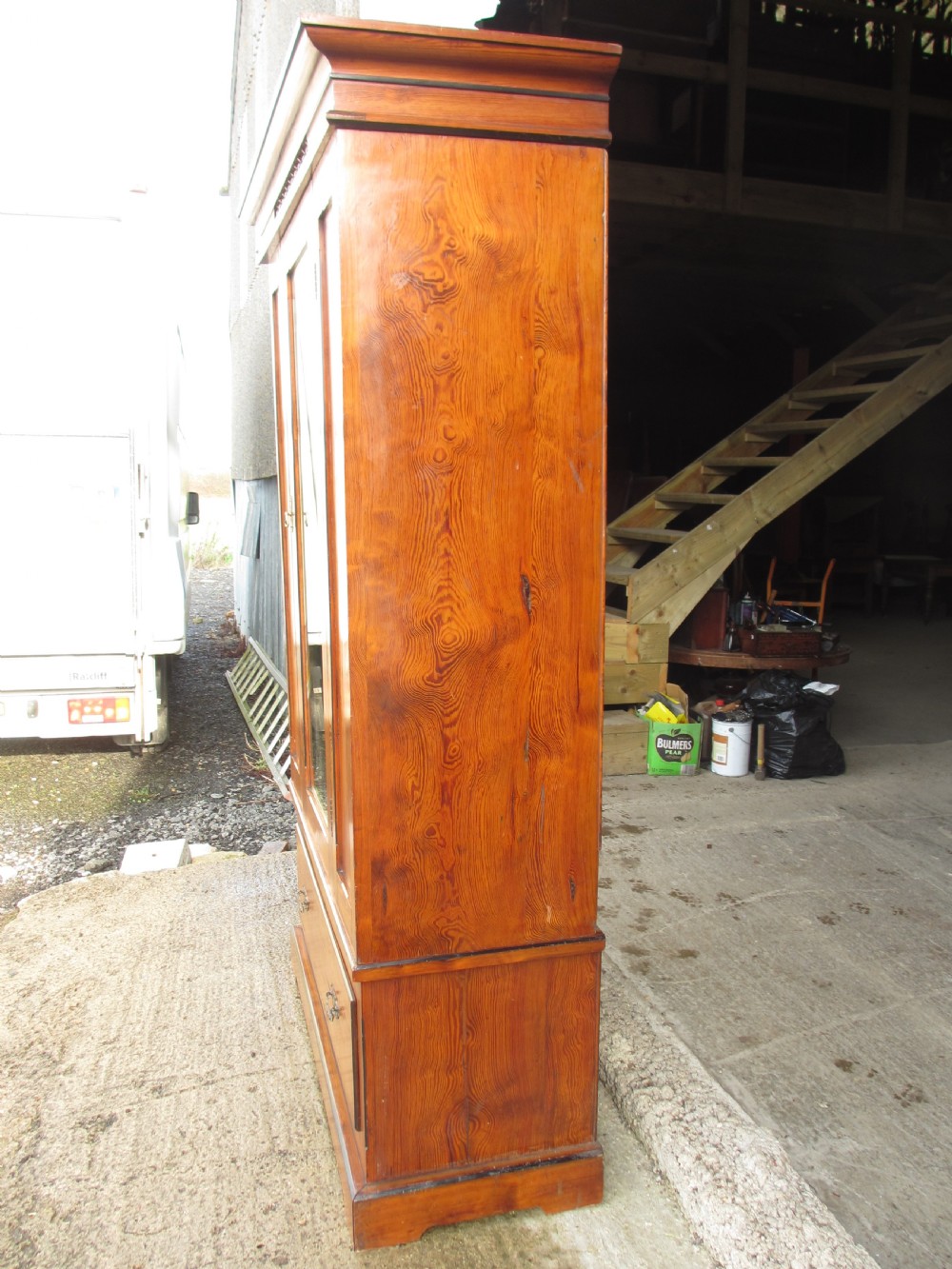 A Victorian pitch pine freestanding wardrobe featuring a central bevelled mirror door, upper spindle gallery, panelled sides, and a single lower drawer. View IX