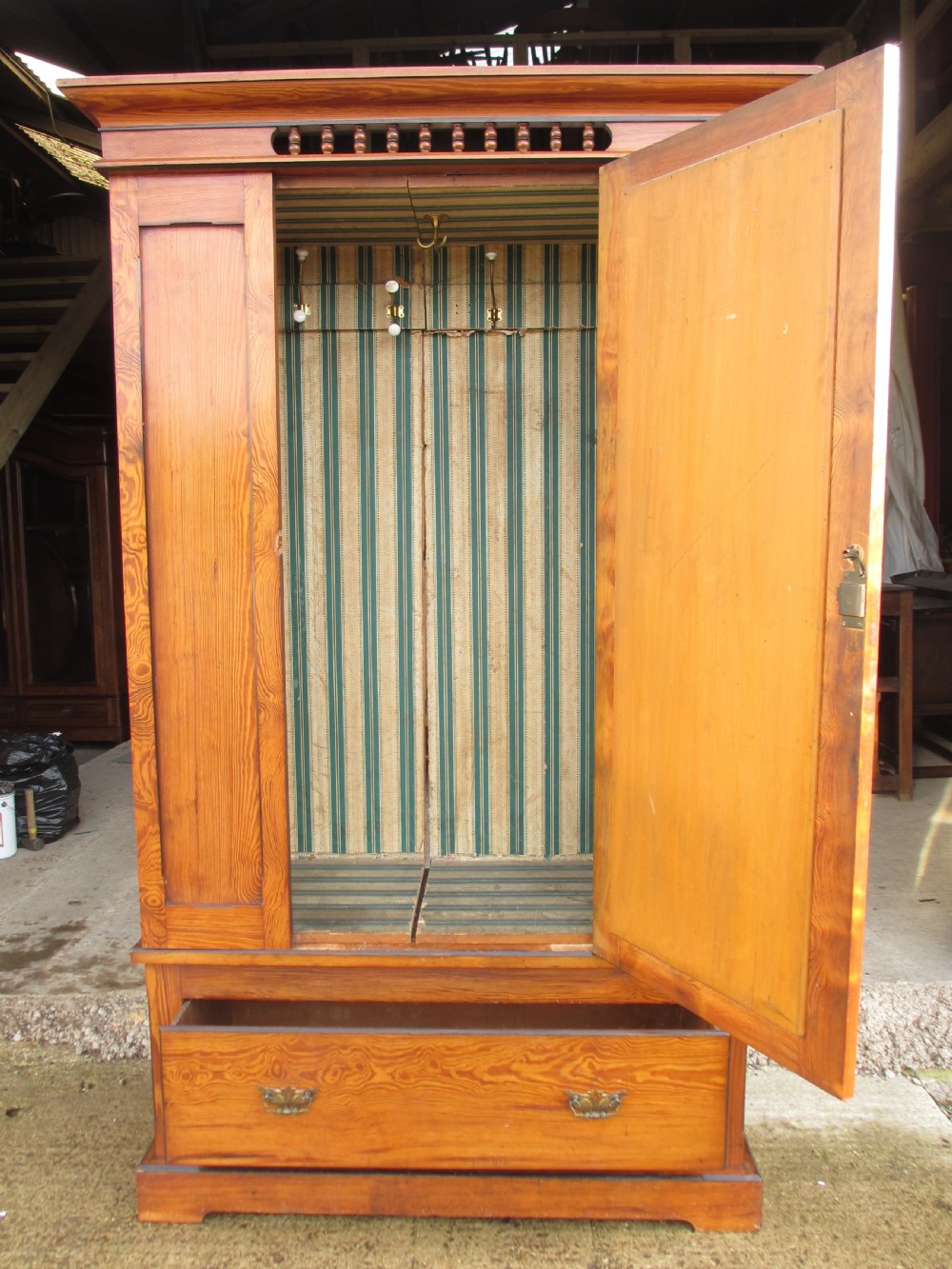 A Victorian pitch pine freestanding wardrobe featuring a central bevelled mirror door, upper spindle gallery, panelled sides, and a single lower drawer. View X