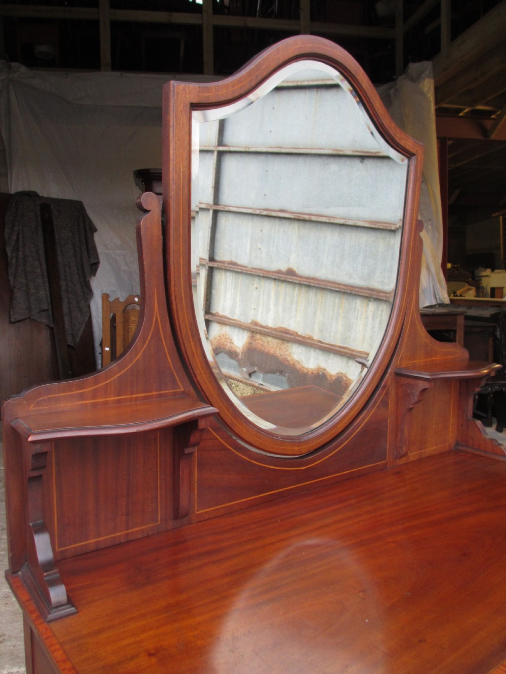 An Edwardian mahogany dressing table featuring a central shield-shaped swing mirror, crossbanded inlay details, three drawers with brass swan-neck handles, tapered legs, and a lower undertier shelf. View V