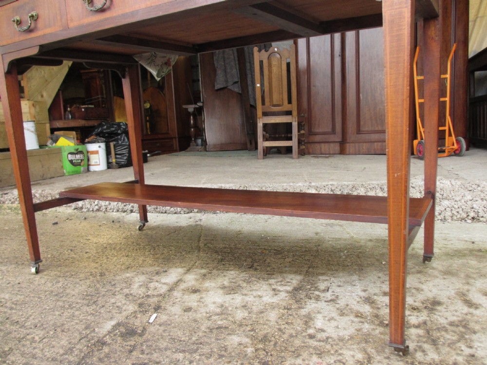 An Edwardian mahogany dressing table featuring a central shield-shaped swing mirror, crossbanded inlay details, three drawers with brass swan-neck handles, tapered legs, and a lower undertier shelf. View VIII