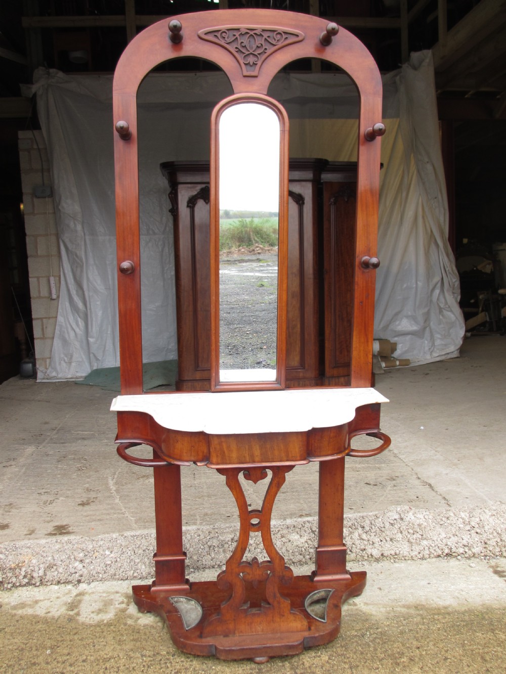 A tall Victorian mahogany hall stand featuring a central mirror, carved top crest, coat pegs, a white marble shelf, and lower umbrella drip trays.