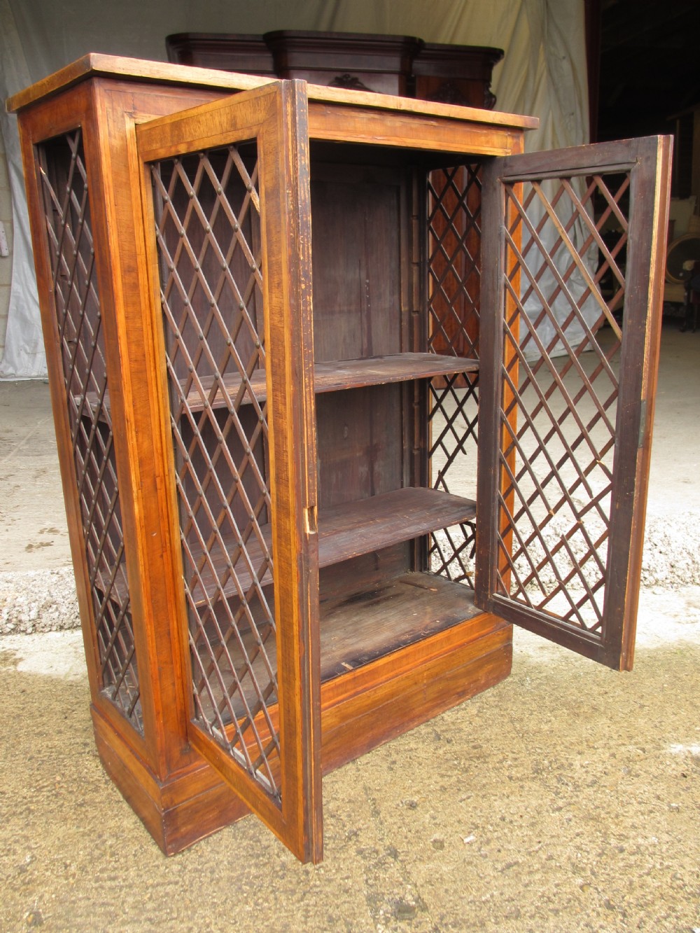 An antique Regency mahogany and walnut bookcase cabinet featuring twin doors and side panels with diamond lattice metal grilles. View II