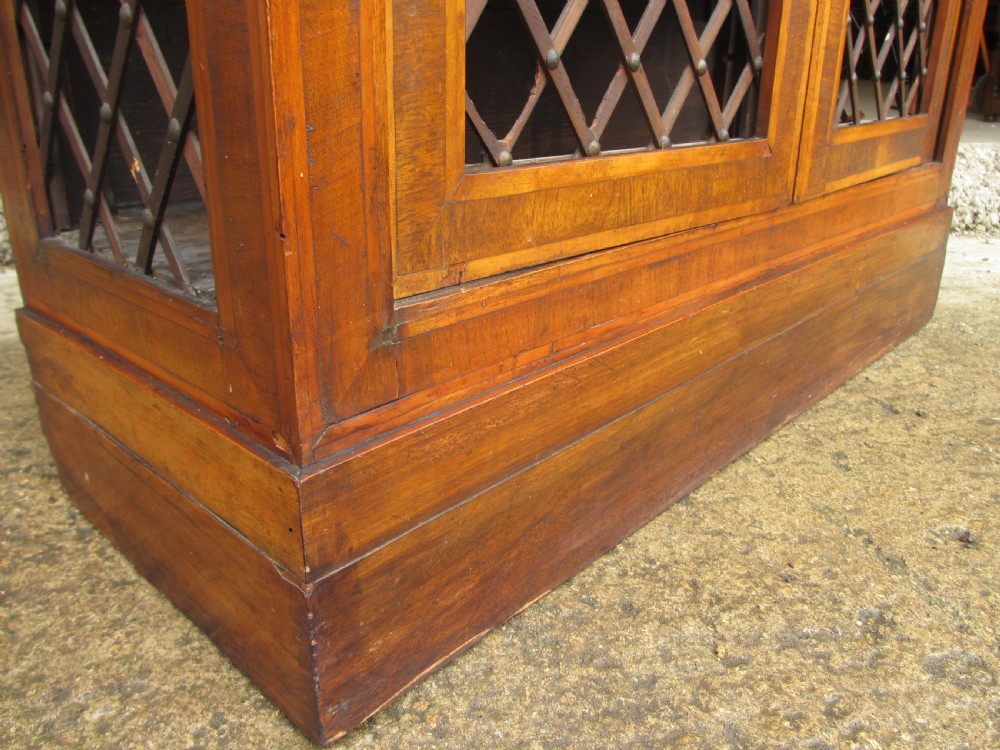 An antique Regency mahogany and walnut bookcase cabinet featuring twin doors and side panels with diamond lattice metal grilles. View IV