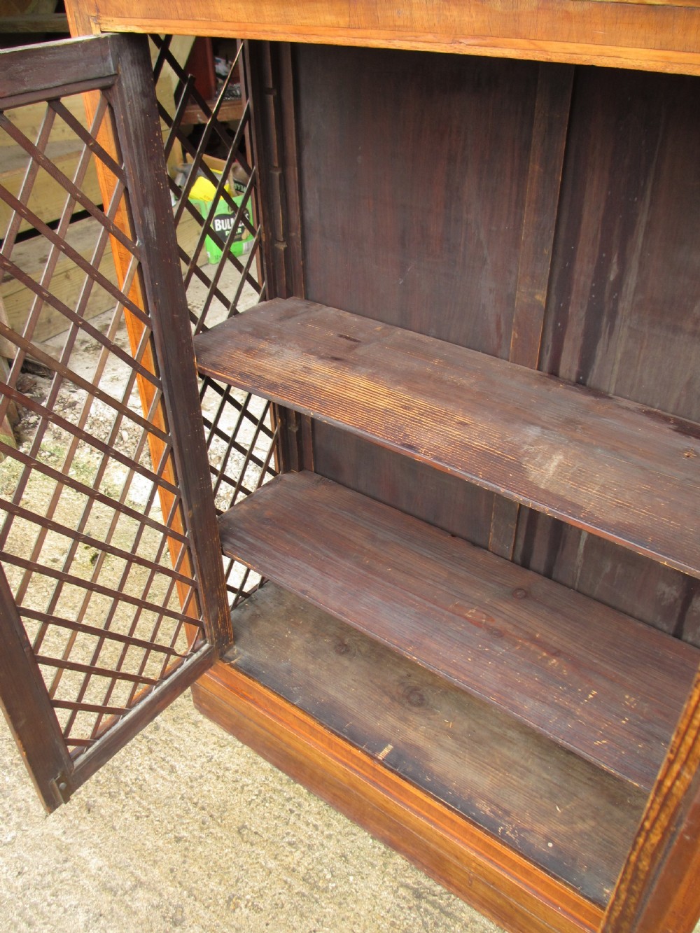 An antique Regency mahogany and walnut bookcase cabinet featuring twin doors and side panels with diamond lattice metal grilles. View V