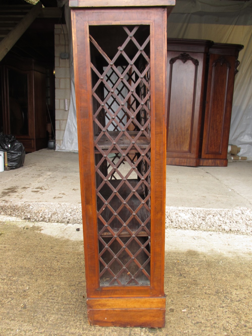 An antique Regency mahogany and walnut bookcase cabinet featuring twin doors and side panels with diamond lattice metal grilles. View VI