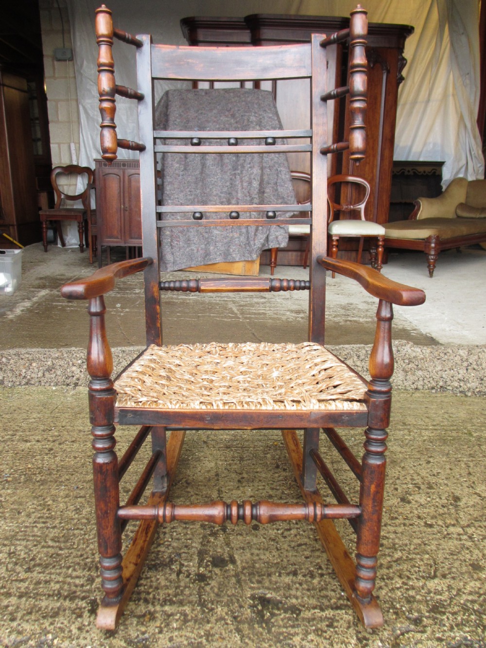 A 19th-century dark beech rocking armchair featuring turned spindle details and a hand-woven seagrass seat.
