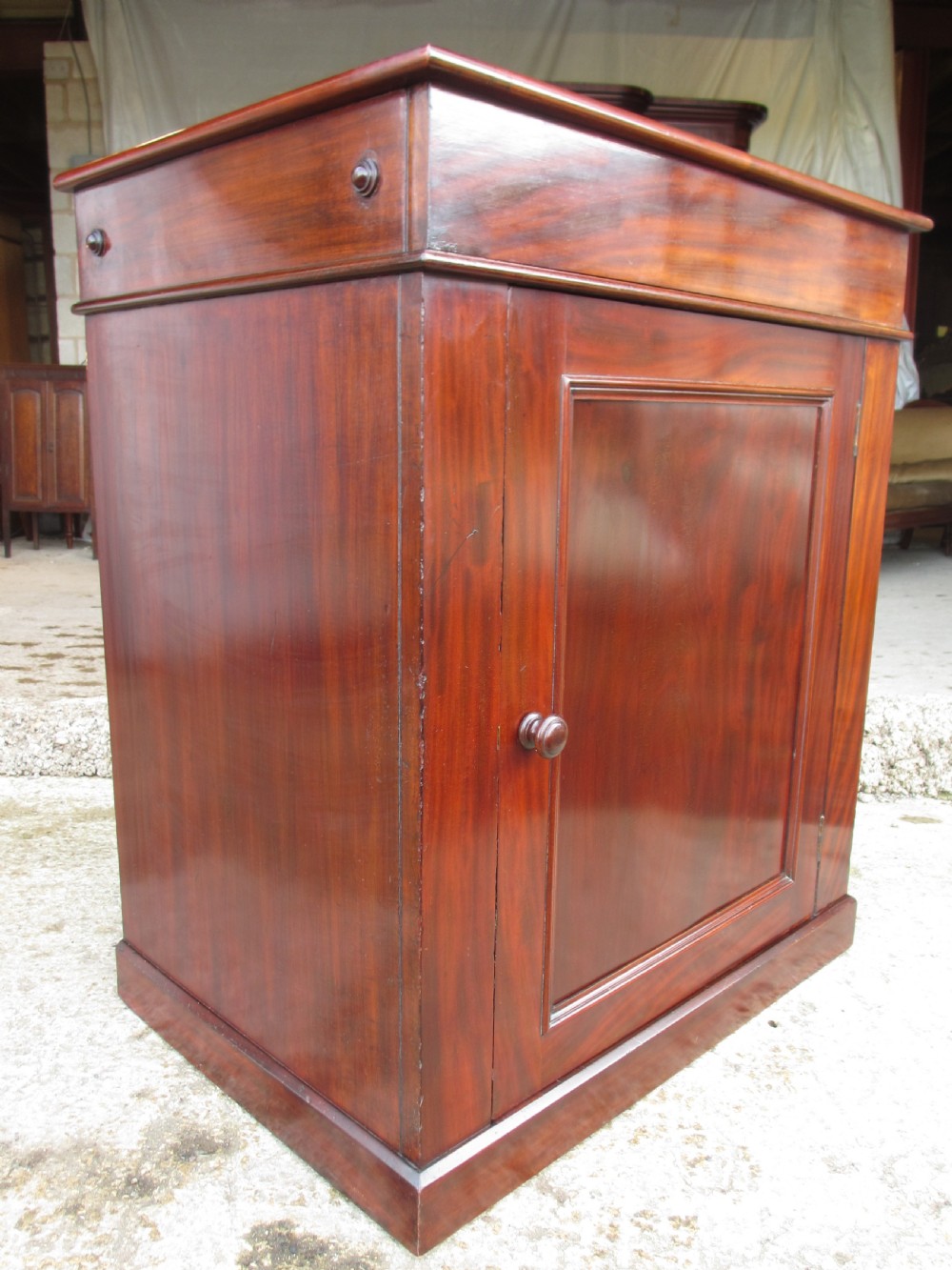 A Victorian flame mahogany washstand cupboard with a single panelled door, wooden knob handle, and plinth base. View V