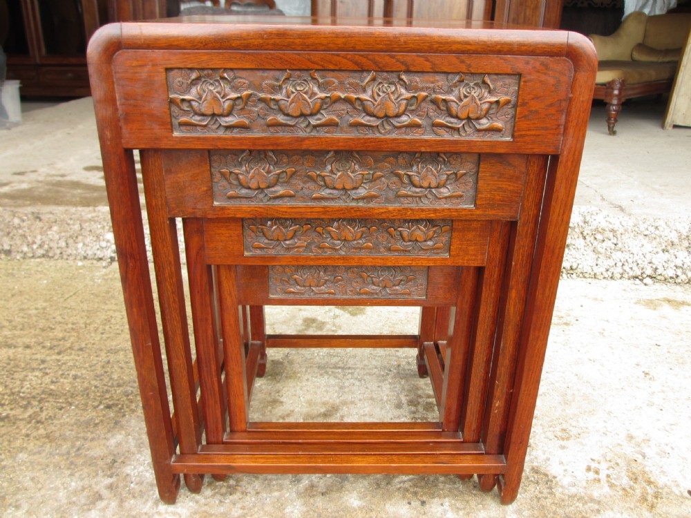 A set of four graduating rosewood side tables nested together, featuring relief-carved lotus friezes and straight legs.