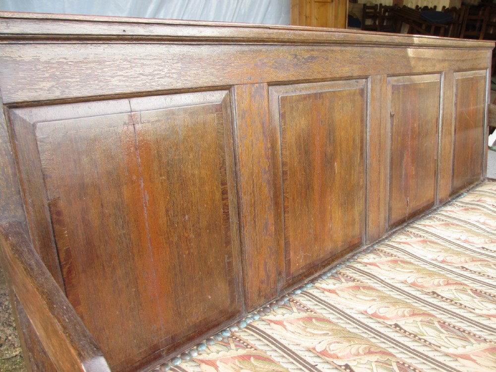 An 18th-century oak settle featuring a four-panel wooden backrest, turned front legs, shaped armrests, and an upholstered patterned seat cushion. View III