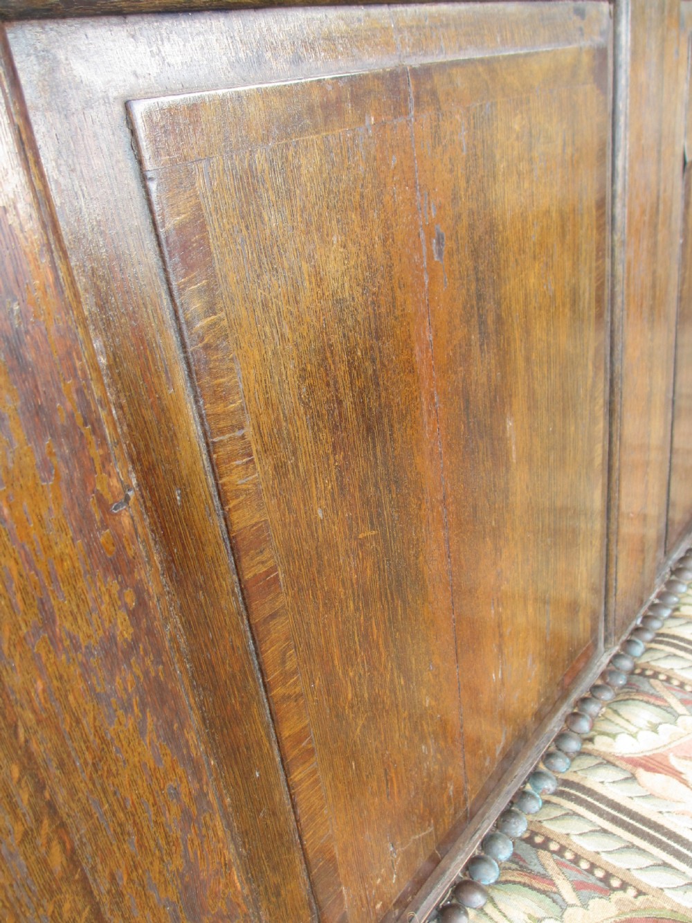 An 18th-century oak settle featuring a four-panel wooden backrest, turned front legs, shaped armrests, and an upholstered patterned seat cushion. View VI