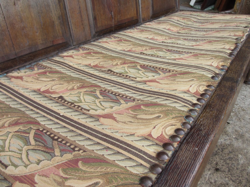 An 18th-century oak settle featuring a four-panel wooden backrest, turned front legs, shaped armrests, and an upholstered patterned seat cushion. View VIII
