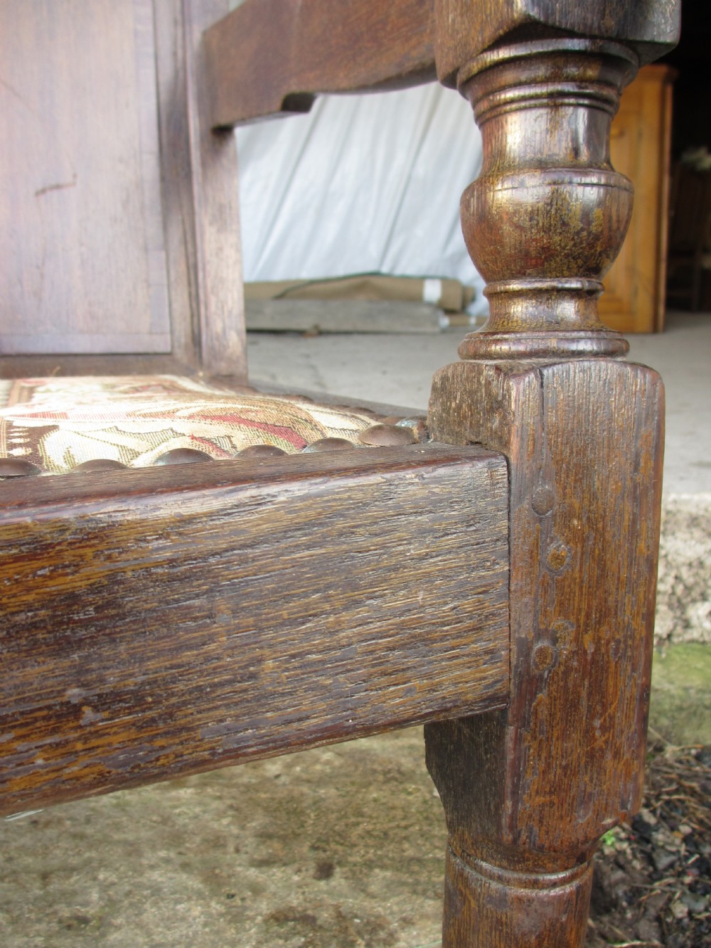 An 18th-century oak settle featuring a four-panel wooden backrest, turned front legs, shaped armrests, and an upholstered patterned seat cushion. View XIII