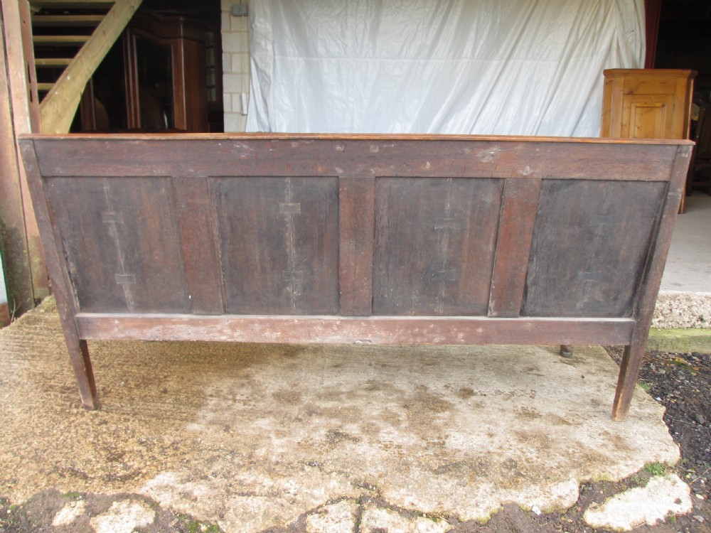 An 18th-century oak settle featuring a four-panel wooden backrest, turned front legs, shaped armrests, and an upholstered patterned seat cushion. View XVI