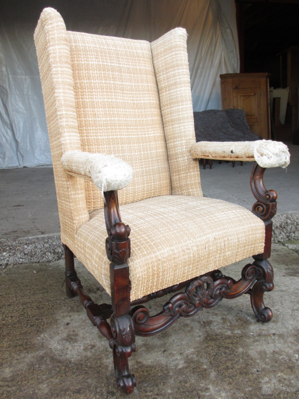 A 19th-century high wingback armchair featuring an intricately carved walnut frame with scroll armrests and neutral woven fabric upholstery. View II