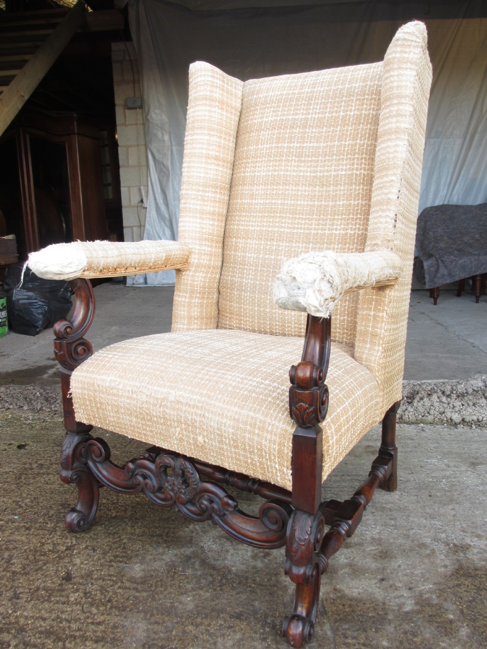 A 19th-century high wingback armchair featuring an intricately carved walnut frame with scroll armrests and neutral woven fabric upholstery. View III