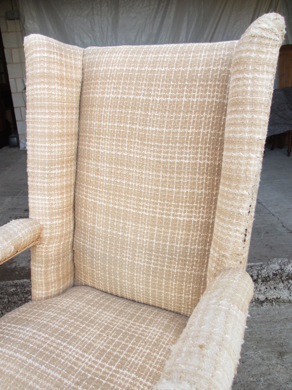 A 19th-century high wingback armchair featuring an intricately carved walnut frame with scroll armrests and neutral woven fabric upholstery. View IV