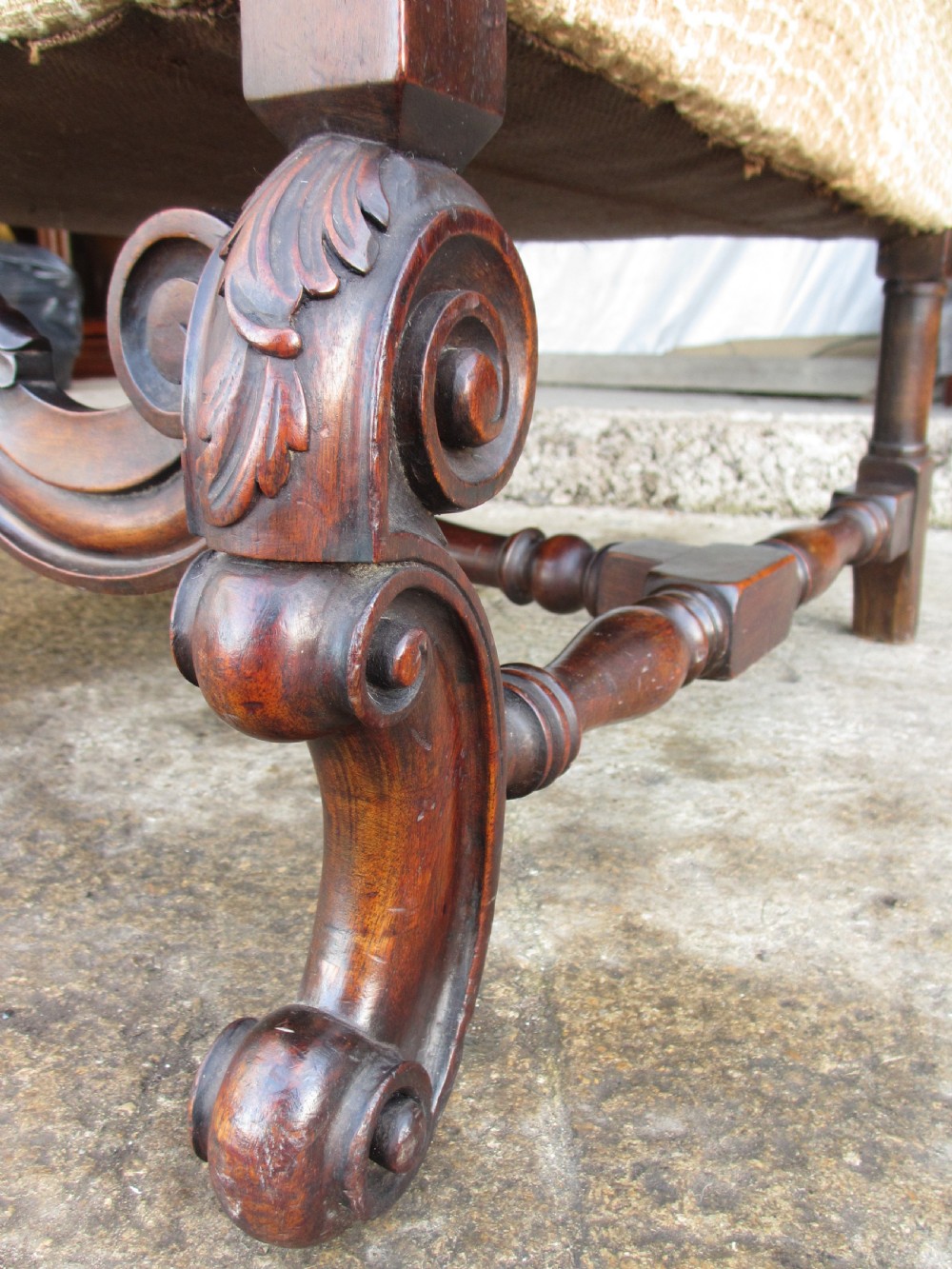 A 19th-century high wingback armchair featuring an intricately carved walnut frame with scroll armrests and neutral woven fabric upholstery. View VII