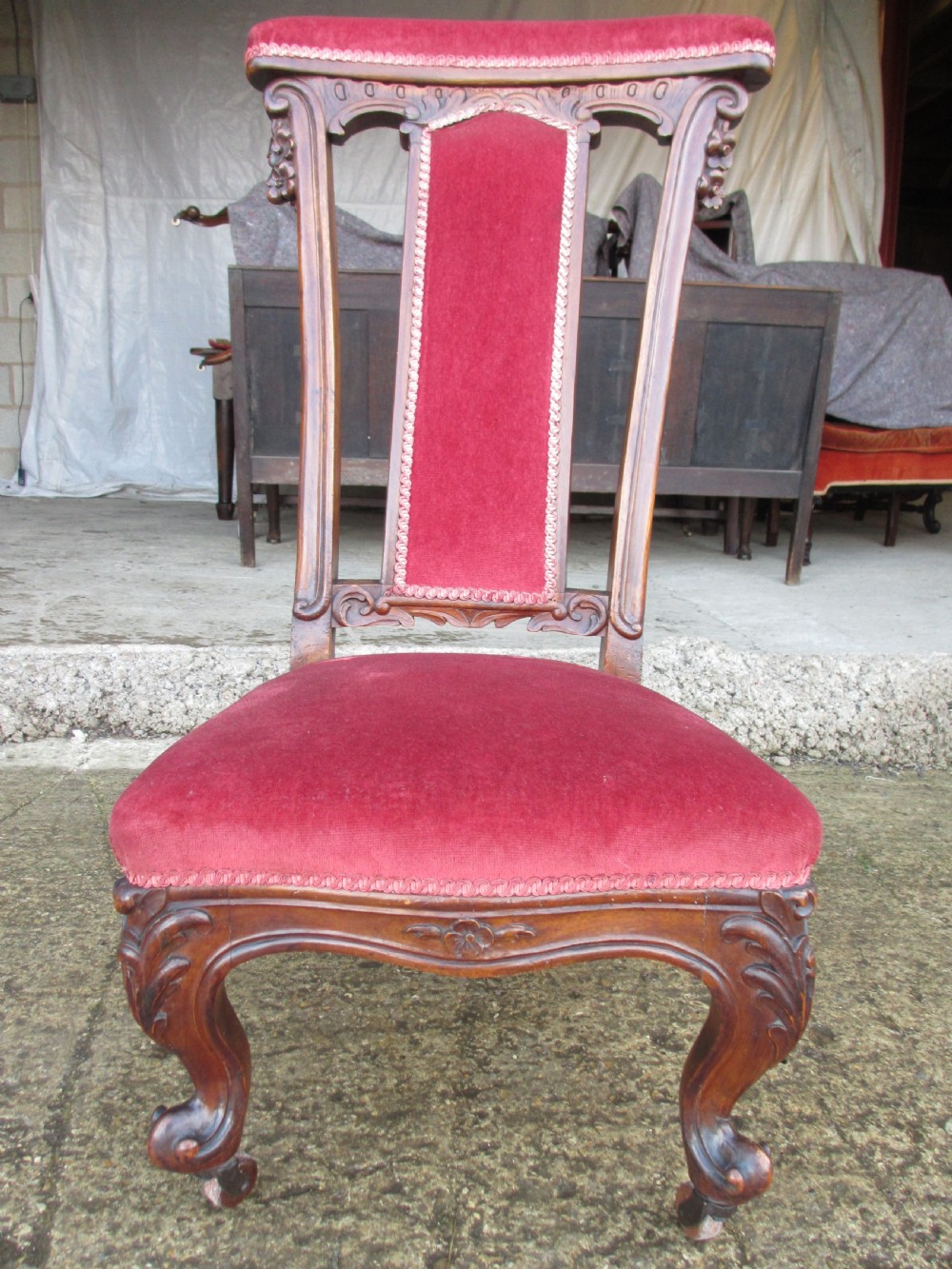 A Victorian carved mahogany prie-dieu chair featuring a tall padded backrest and low seat upholstered in crimson velvet with carved cabriole front legs.