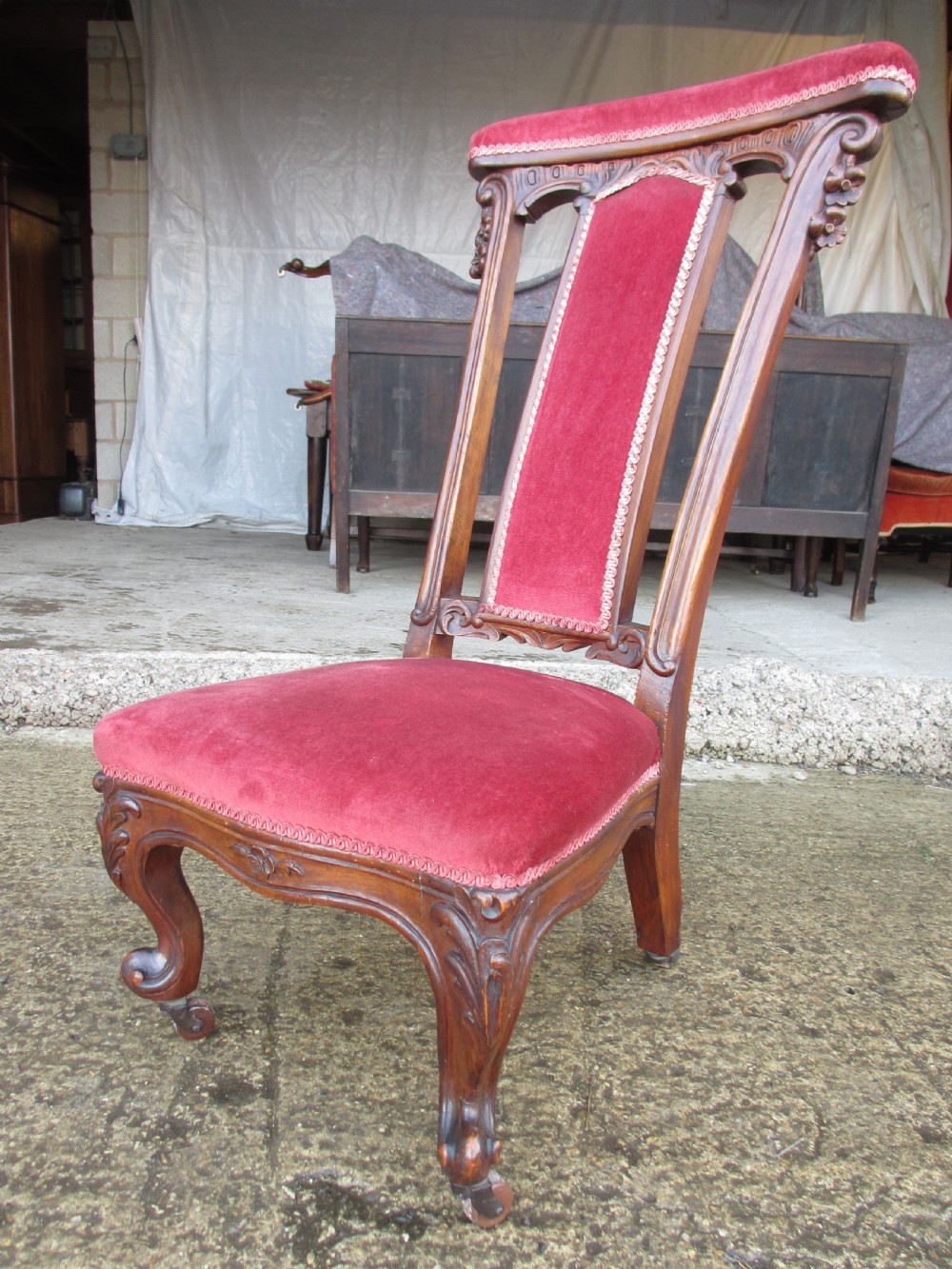 A Victorian carved mahogany prie-dieu chair featuring a tall padded backrest and low seat upholstered in crimson velvet with carved cabriole front legs. View II