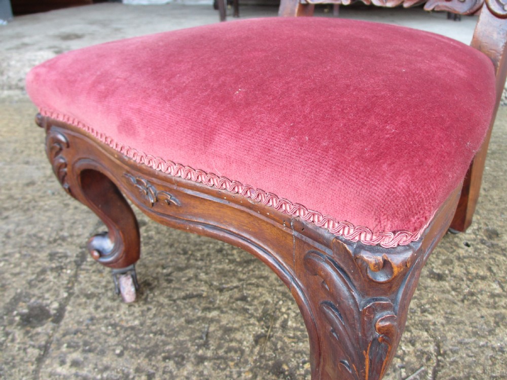 A Victorian carved mahogany prie-dieu chair featuring a tall padded backrest and low seat upholstered in crimson velvet with carved cabriole front legs. View V