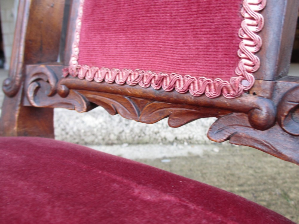A Victorian carved mahogany prie-dieu chair featuring a tall padded backrest and low seat upholstered in crimson velvet with carved cabriole front legs. View X
