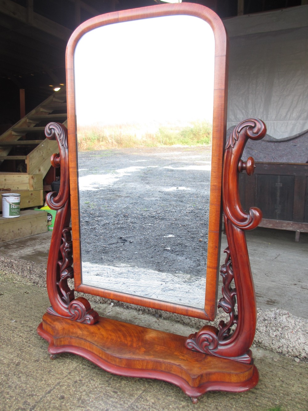 A 19th-century flame mahogany cheval mirror featuring an arched tilting frame suspended between carved scroll supports on a serpentine base. View V