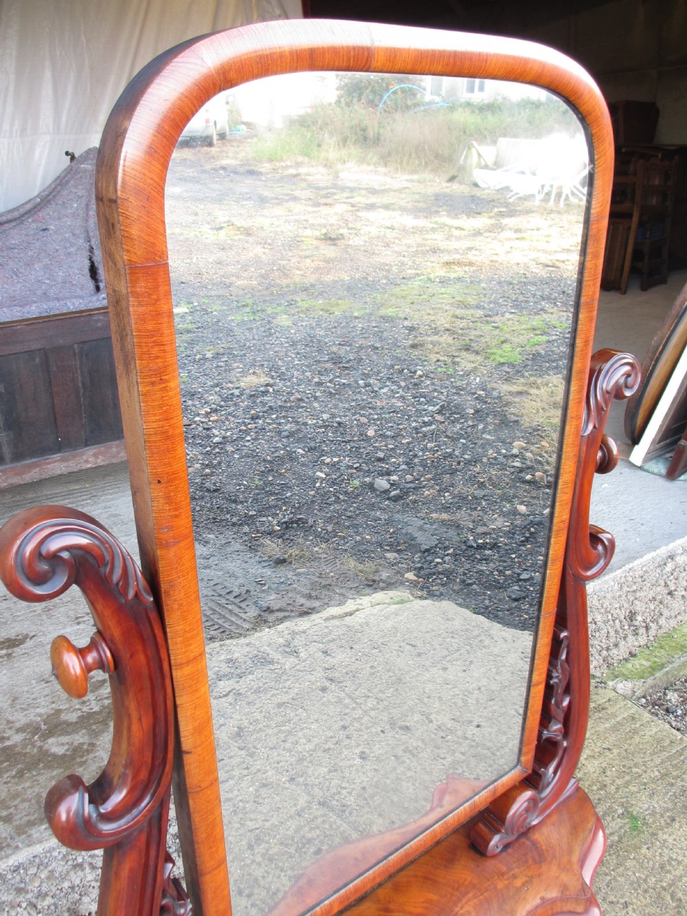 A 19th-century flame mahogany cheval mirror featuring an arched tilting frame suspended between carved scroll supports on a serpentine base. View VI