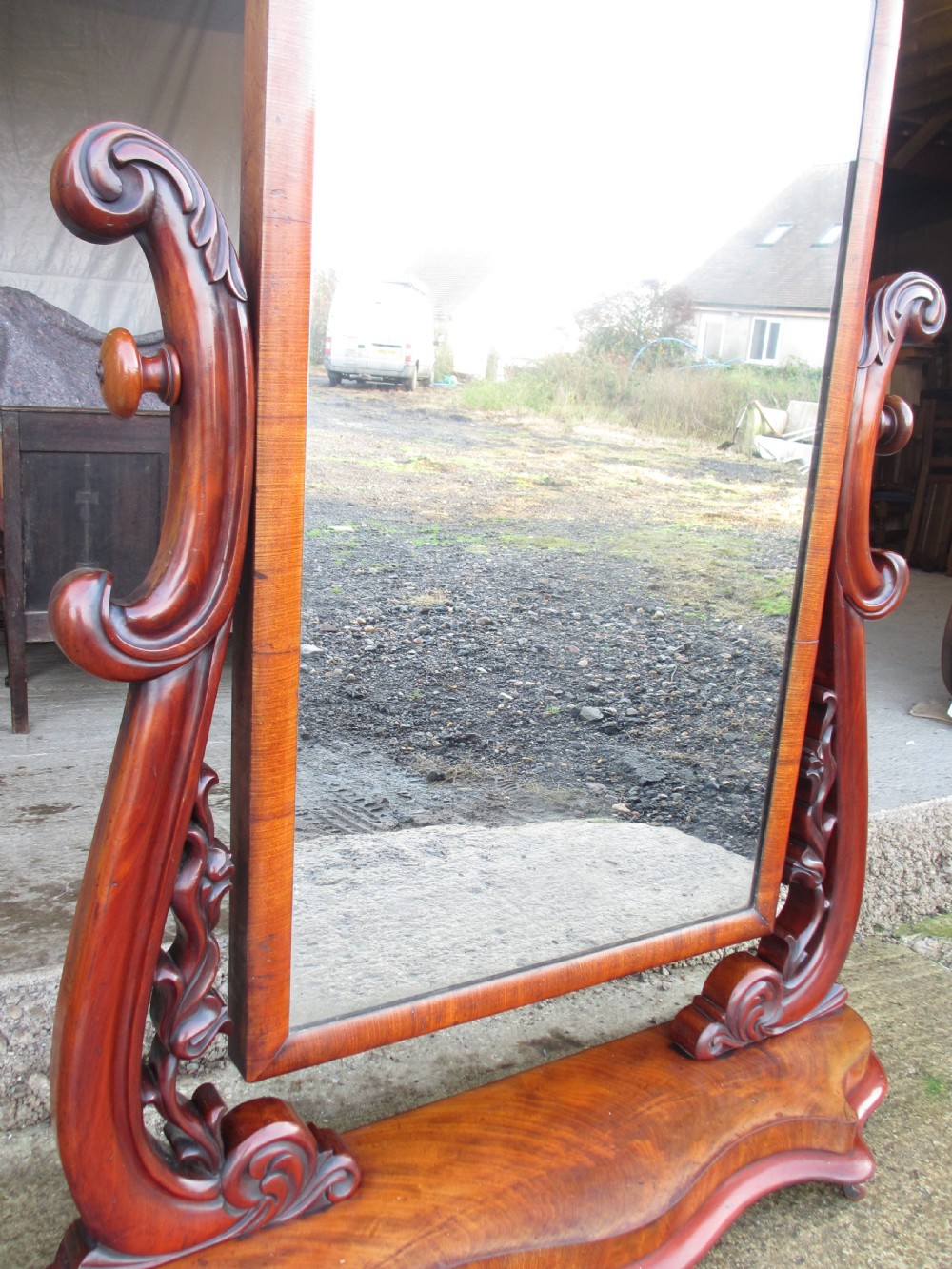 A 19th-century flame mahogany cheval mirror featuring an arched tilting frame suspended between carved scroll supports on a serpentine base. View VII