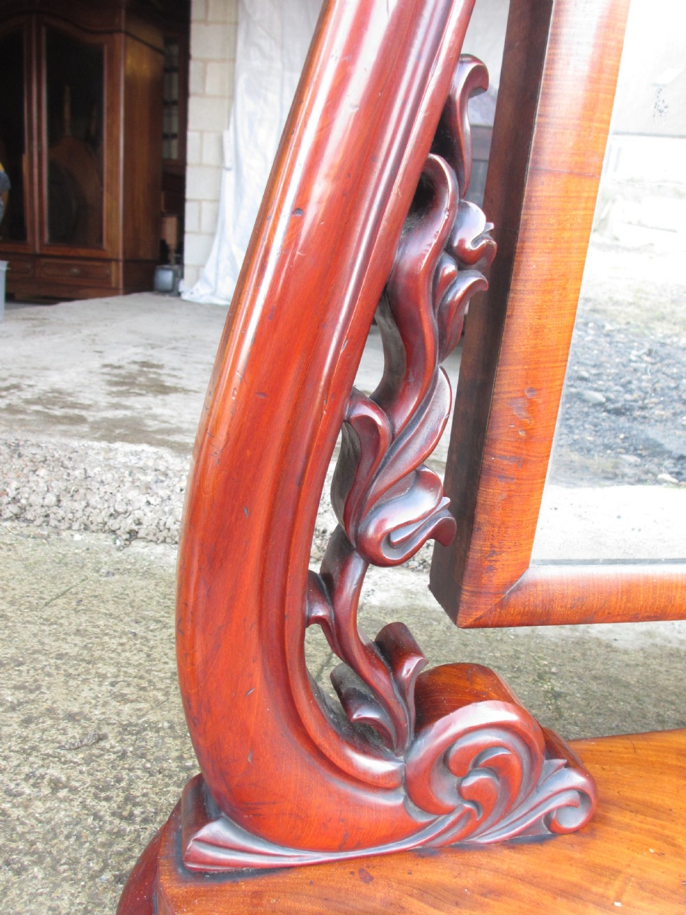 A 19th-century flame mahogany cheval mirror featuring an arched tilting frame suspended between carved scroll supports on a serpentine base. View XI
