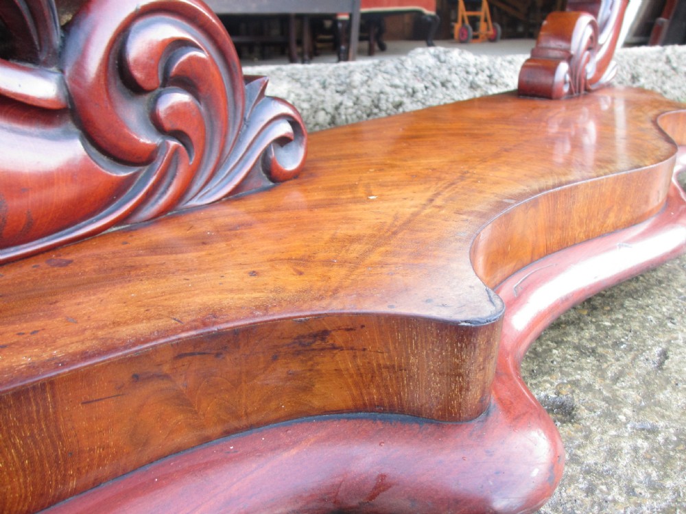 A 19th-century flame mahogany cheval mirror featuring an arched tilting frame suspended between carved scroll supports on a serpentine base. View XII
