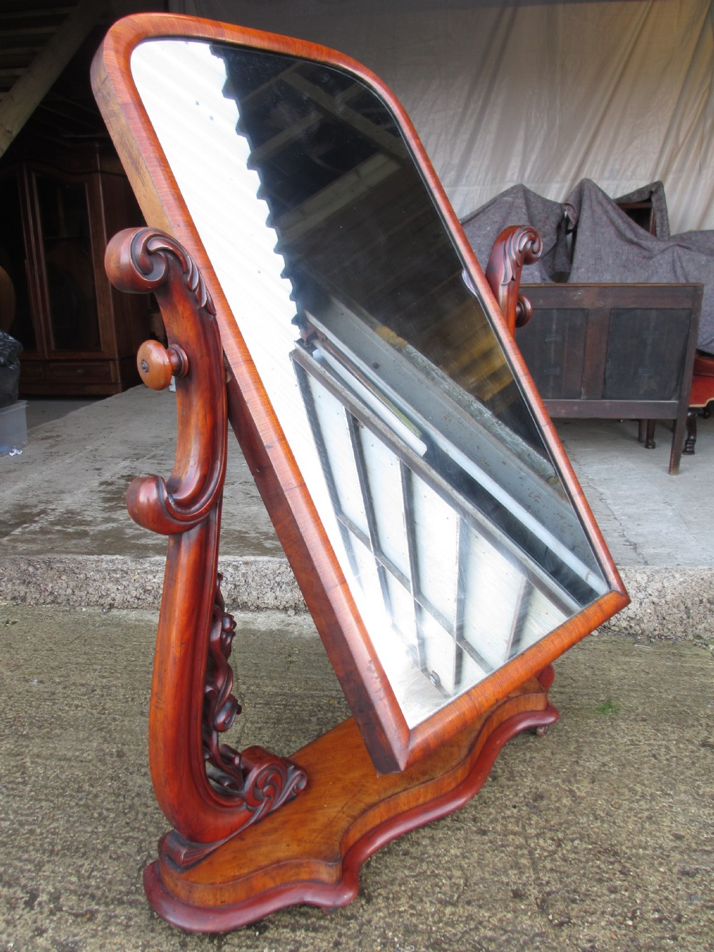 A 19th-century flame mahogany cheval mirror featuring an arched tilting frame suspended between carved scroll supports on a serpentine base. View XIII