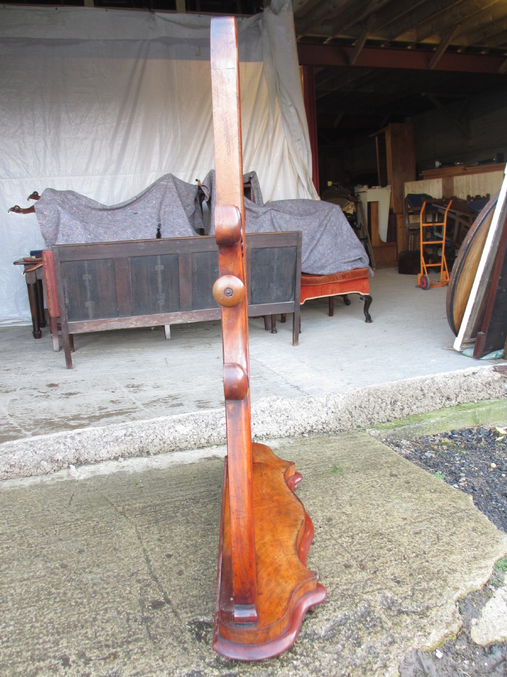 A 19th-century flame mahogany cheval mirror featuring an arched tilting frame suspended between carved scroll supports on a serpentine base. View XIV