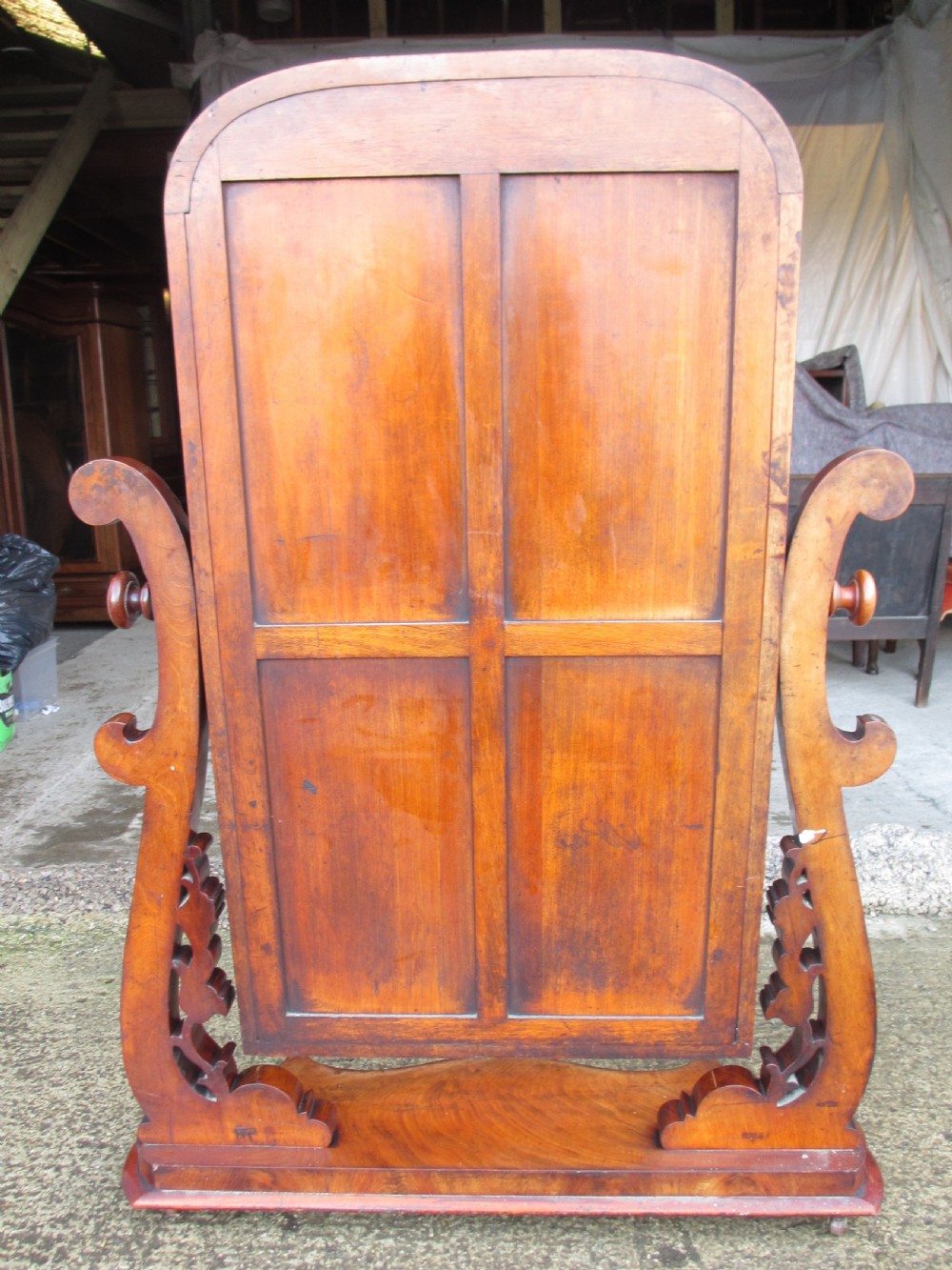 A 19th-century flame mahogany cheval mirror featuring an arched tilting frame suspended between carved scroll supports on a serpentine base. View XV