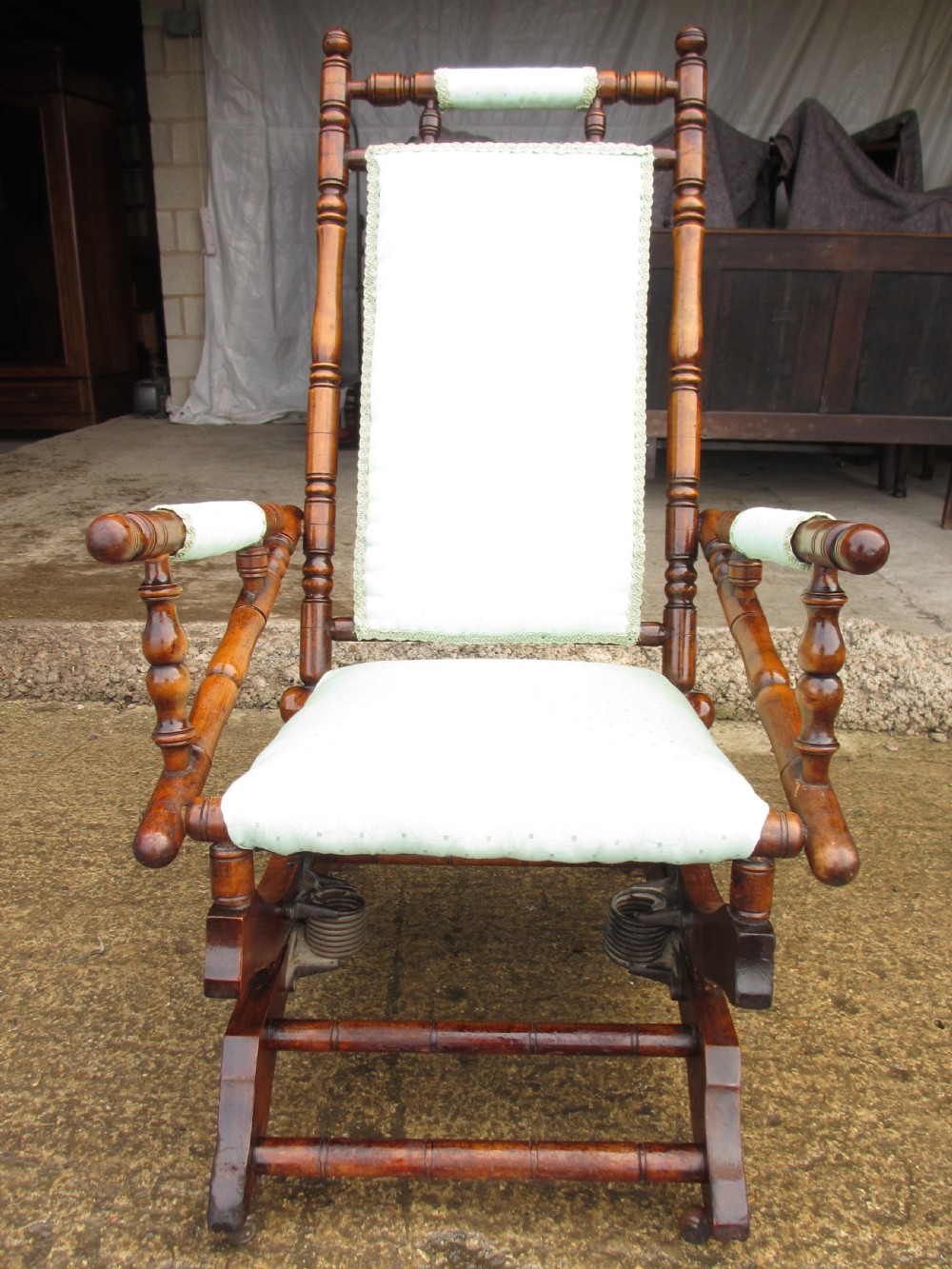 A 19th-century American platform rocking chair crafted from turned beechwood with pale green fabric upholstery on a stationary spring base.