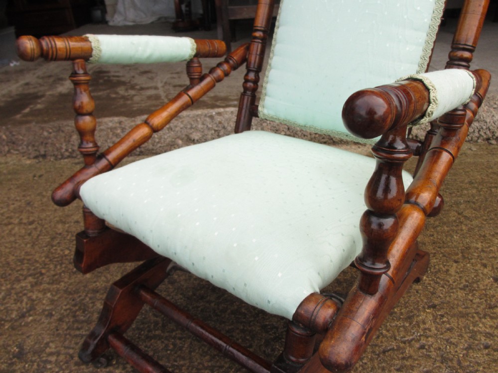A 19th-century American platform rocking chair crafted from turned beechwood with pale green fabric upholstery on a stationary spring base. View V