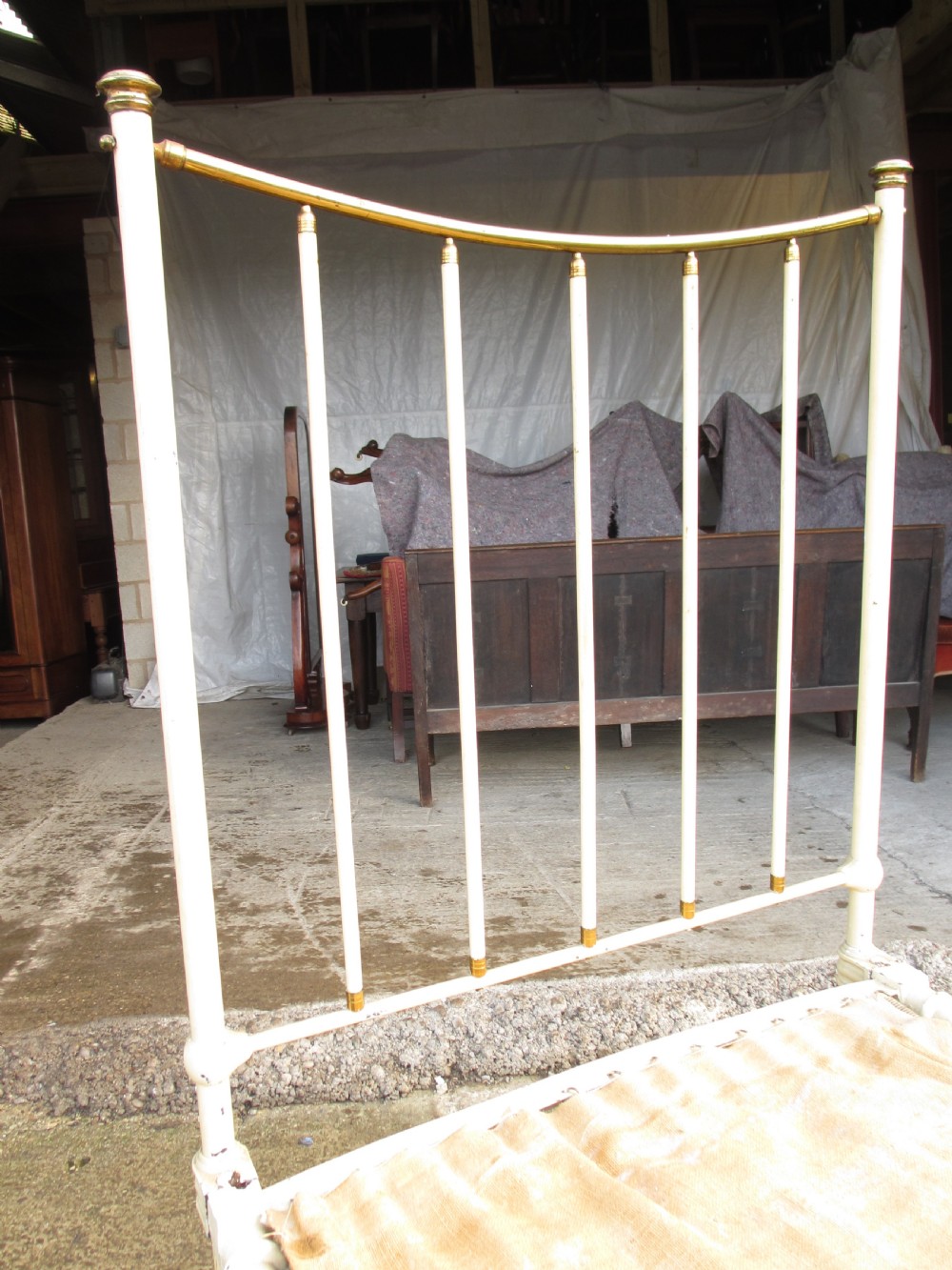 An antique Victorian single bedstead featuring a painted off-white iron frame, brass top rails, vertical spindles, and castors. View VI