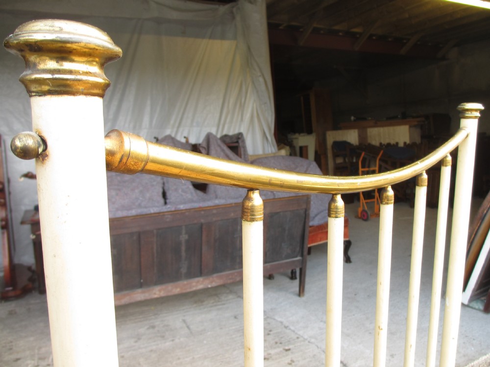 An antique Victorian single bedstead featuring a painted off-white iron frame, brass top rails, vertical spindles, and castors. View VIII