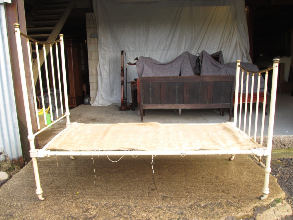 An antique Victorian single bedstead featuring a painted off-white iron frame, brass top rails, vertical spindles, and castors. View XV