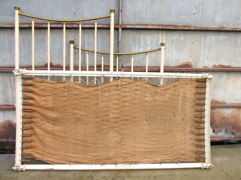 An antique Victorian single bedstead featuring a painted off-white iron frame, brass top rails, vertical spindles, and castors. View XVI