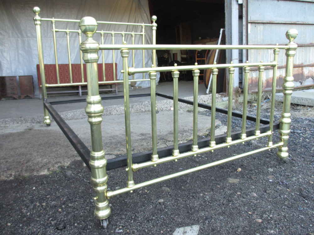A Victorian double bedstead constructed from polished tubular brass with vertical spindles, turned posts, spherical finials, and an iron support frame on castors.