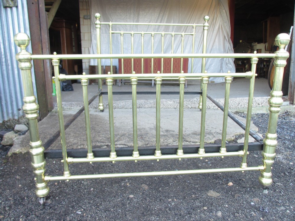 A Victorian double bedstead constructed from polished tubular brass with vertical spindles, turned posts, spherical finials, and an iron support frame on castors. View II