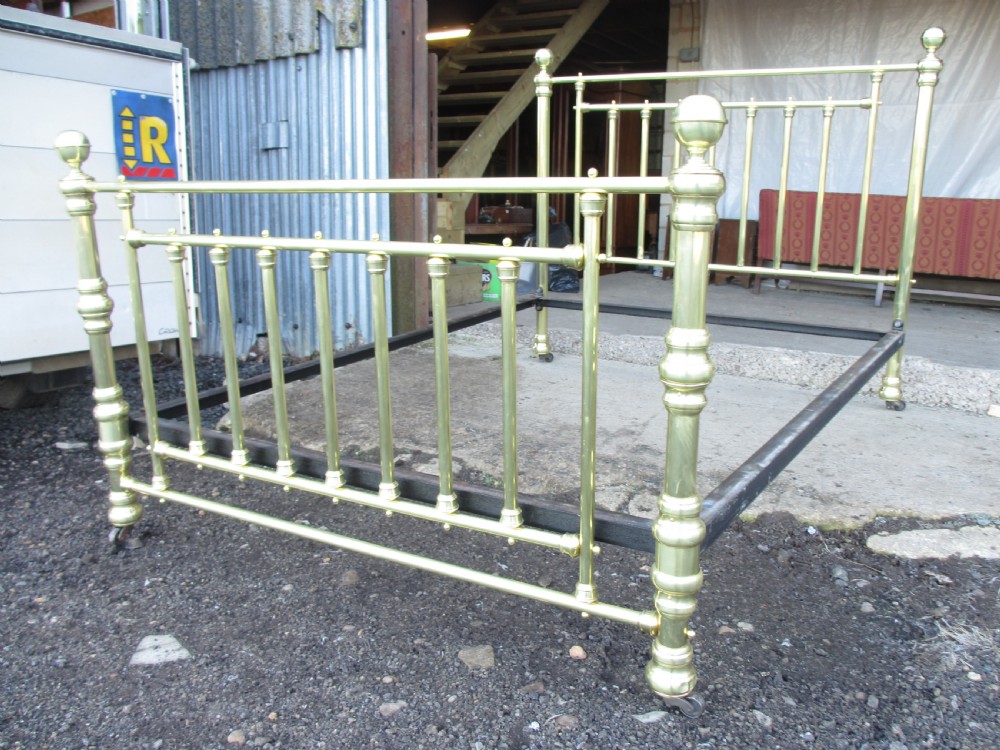 A Victorian double bedstead constructed from polished tubular brass with vertical spindles, turned posts, spherical finials, and an iron support frame on castors. View III