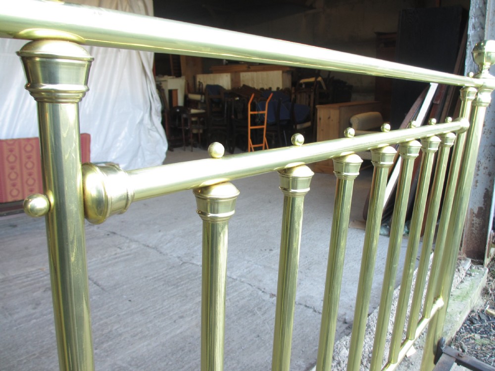 A Victorian double bedstead constructed from polished tubular brass with vertical spindles, turned posts, spherical finials, and an iron support frame on castors. View IV