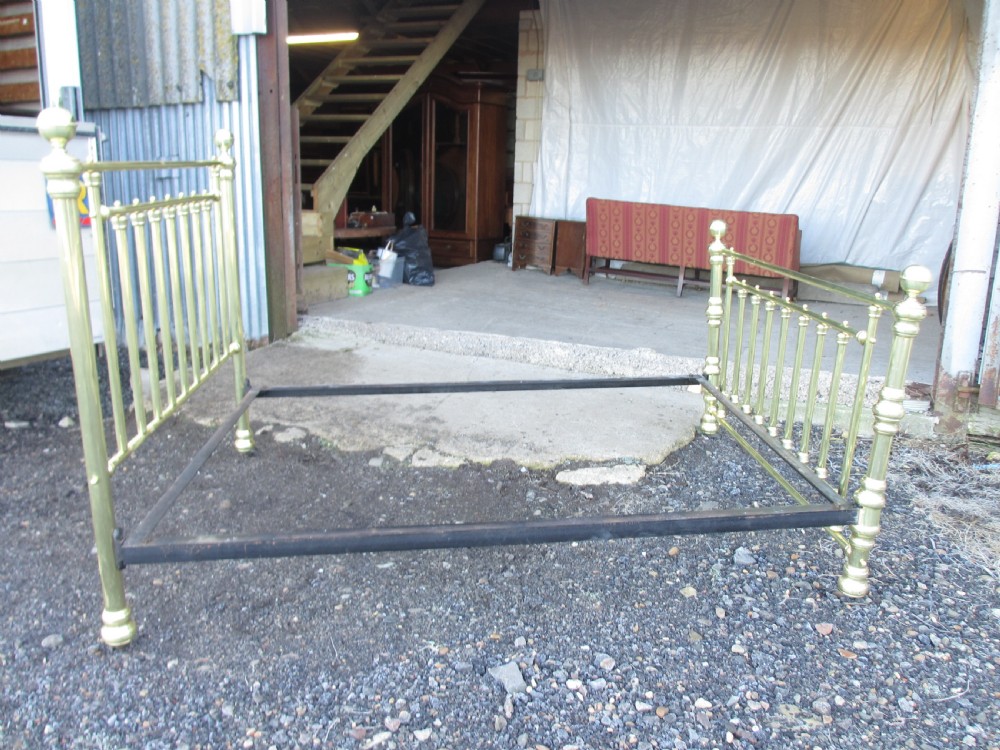 A Victorian double bedstead constructed from polished tubular brass with vertical spindles, turned posts, spherical finials, and an iron support frame on castors. View V